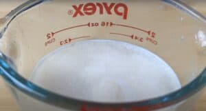 Pyrex measuring cup with frothy mixture, accurate measurement for baking or cooking recipes, two-cup capacity.